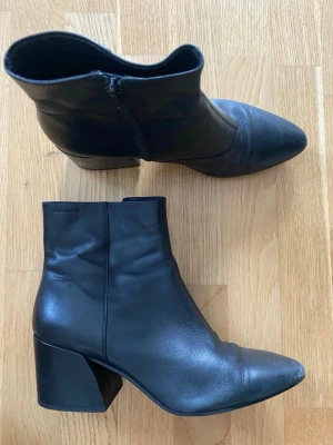 Svarta stövletter med klack - Snygga svarta stövletter i skinn med spetsig tå och bred klack. Dragkedja på insidan för enkel påtagning. Perfekta till jeans eller klänning för en trendig look.
