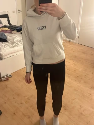Vit hoodie från Polo Ralph Lauren - Snygg vit hoodie från Polo Ralph Lauren med svart logga på bröstet. Klassisk känguruficka framtill och huva. Perfekt för en chill och stilren look. Mjuk bomullskänsla och ribbade muddar vid ärmslut och nederkant. Strl M men e som XS-S