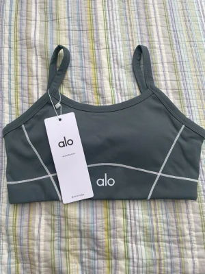 Grått träningsset från Alo Yoga - Snyggt träningsset från Alo Yoga i grått med vita sömdetaljer. Setet består av en sport-bh med tunna axelband och matchande tights med hög midja och praktiska fickor. Materialet är stretchigt och andas, perfekt för yoga eller gym.