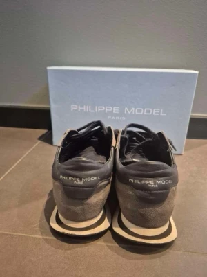 Philippe Model svarta sneakers - Philippe Model sneakers  Säljer ett par stilrena Philippe Model sneakers i svart/grå färgkombination med den ikoniska sköldloggan. Premiumkänsla med snygg mix av material och en modell som fungerar lika bra till vardag som en mer uppklädd outfit. Kommer med originalbox. Använda med normalt slitage enligt bilderna men fortfarande mycket kvar att ge. Säljes då de inte kommer till användning. Passa på att fynda ett par tidlösa designersneakers. Sko boxen följer såklart med 