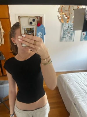 Svart croppad topp med öppen rygg - Snygg svart croppad topp med korta ärmar och öppen rygg. Perfekt för dig som vill ha en enkel men ändå trendig look. Toppens tighta passform framhäver figuren och den är lätt att matcha med olika outfits.