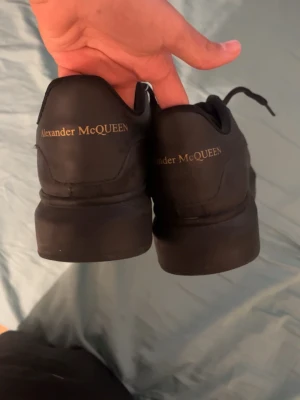 Svarta Alexander McQueen sneakers - Stilrena svarta sneakers från Alexander McQueen med guldtext på hälen. Skorna har en chunky sula och är tillverkade i läder med klassisk låg profil. Perfekta för dig som vill ha en clean och lyxig look med streetkänsla.