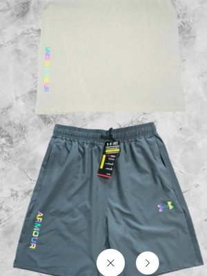 Grå shorts från Under Armour - Snygga grå shorts från Under Armour med elastisk midja och snörning. Loggan och texten 'ARMOUR' i regnbågsfärger ger en cool touch. Perfekta för träning eller chill. Lätta och bekväma med sidofickor. Pris kan diskuteras vid snabb affär 