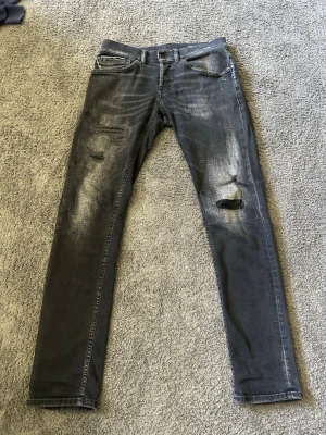 Dondup - Säljer ett par grå skinny jeans från Dondup med slitningar och hål på benen. Jeansen har fem fickor, dragkedjegylf och en cool tvättad look. Perfekta för dig som gillar en edgy och trendig stil.