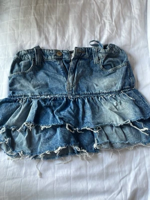 Jeanskjol från Gina Tricot - Säljer en jeankjol i ljusblå  från Gina Tricot. Modellen har volangdetaljer och råa kanter för en trendig look. Kjolen har två fickor i fram  och dragkedja fram. Perfekt för dig som gillar en avslappnad men cool stil. Kjolen har inga fickor ibak. Använd fåtal gånger 