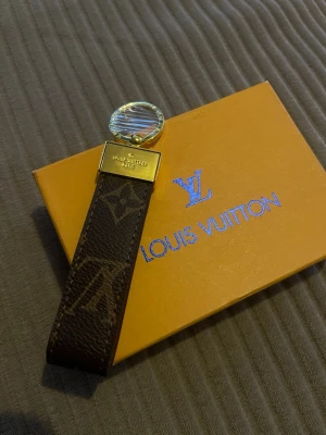  Vuitton håraccessoar monogram - Lyxig håraccessoar från  Vuitton i klassiskt brunt monogrammönster. Detaljer i guldmetall och en rund transparent dekoration upptill. Perfekt för att ge din frisyr en exklusiv touch och visa upp din stil.