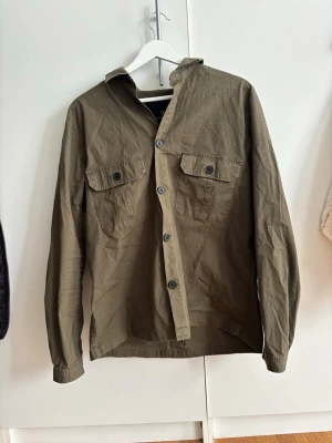 Grön overshirt  - Snygg olivgrön skjorta med två bröstfickor och knappar framtill. Storlek M och modellen är 182 och väger 77 ish || frågor?
