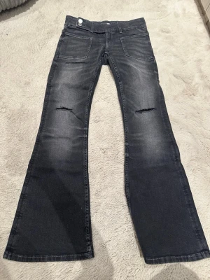 Mörkgrå bootcut jeans med slitningar från Gina tricot - Säljer ett par mörkgrå bootcut jeans med slitningar över knäna och snygg tvätt. Jeansen har framfickor, bakfickor och vida ben. Perfekta för dig som gillar en avslappnad men trendig look. Helt sprillans nya har inte använt någon gång. Men rensar nu ut dem 