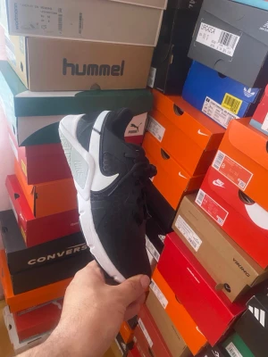 Svarta Nike sneakers med vit sula - Snygga svarta Nike sneakers med vit sula och vit swoosh på sidan. Ovandelen har ett diskret hexagonmönster och skon har klassisk låg profil. Perfekta för dig som vill ha en stilren och sportig look. Skon är tillverkad i textil och syntetmaterial.