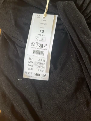 Svart tie singlet med knyt XS - Svart ärmlös tie singlet med smala axelband och knyt framtill. Toppen har en luftig passform och är perfekt för varma dagar. Tillverkad i mjukt material som känns skönt mot huden.