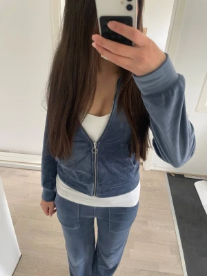 Blå velourset med zip och hoodie - Säljer ett mjukt och skönt set i blå velour, bestående av zip-jacka med fickor och huva samt matchande byxor med raka ben. Perfekt för chill eller mys hemma. Jackan har silverfärgad dragkedja och byxorna har fickor bak och framtill 