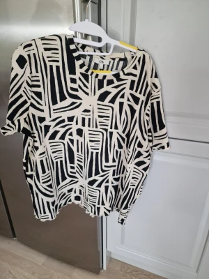 Svartvit mönstrad t-shirt från C&A - Cool svartvit t-shirt från C&A i storlek XL med grafiskt mönster. T-shirten har rund hals. Skönt material. Köpte från Spanien.