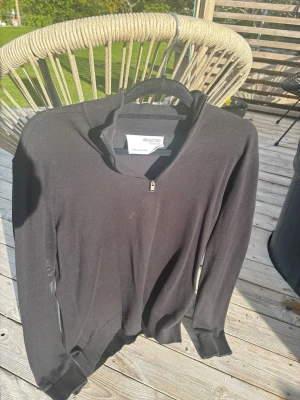 Svart ziptröja från Selected Homme - Snygg svart långärmad ziptröja från Selected Homme. Tröjan har en halv dragkedja vid halsen och ribbade muddar vid ärmslut och nederkant. Perfekt för en clean och stilren look.