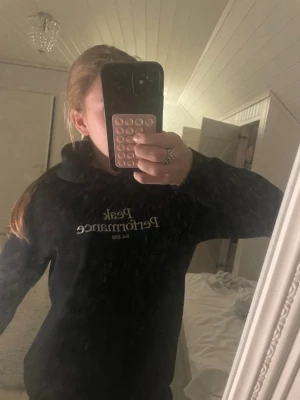 Svart hoodie från Peak Performance - Säljer en svart hoodie från Peak Performance med vit logga på bröstet. Hoodien har en klassisk huva och lång ärm, perfekt för en avslappnad och stilren look.