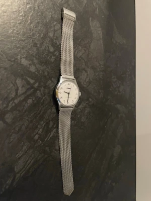 Klassisk silverfärgad klocka Hobbex  - Stilren klocka från Hobbex i silver med mesh-armband och rund urtavla. Urtavlan är vit med tydliga svarta siffror och Fossil-logga. Klockan har en minimalistisk design som passar till många olika stilar. (Funkar ej!!, behöver nytt batteri.)