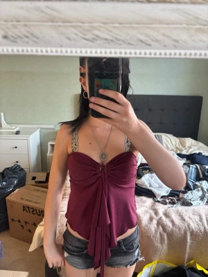 Vinröd bandeau topp från Ally - Säljer en vinröd bandeau topp från Ally med snygg knytning framtill. Toppen är ärmlös och har en croppad passform som ger en cool och trendig look. Perfekt för dig som vill sticka ut med en unik detalj framtill.
