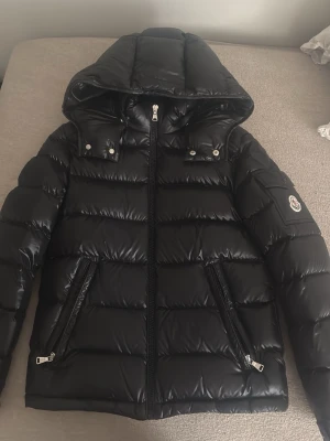 new maya jacket moncler  -  stlrk 152 men passar på 158 också( kvitto finns)  Äkta new maya jacket  svart  från Moncler med glansig finish, huva och två dragkedjefickor framtill. Klassisk Moncler-logga på ärmen och quiltad design. Perfekt för kalla vinterdagar och riktigt varm tack vare dunfyllningen.