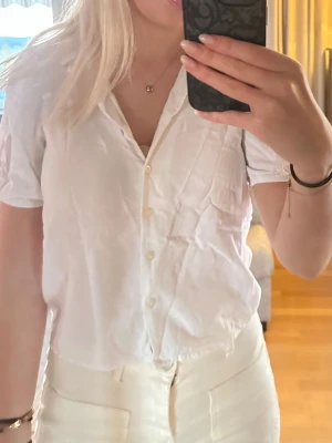 Vit kortärmad skjorta med knappar - Snygg vit skjorta med korta ärmar och klassisk krage. Skjortan har knäppning framtill och en bröstficka. Perfekt till sommarens outfits och enkel att styla med olika plagg.