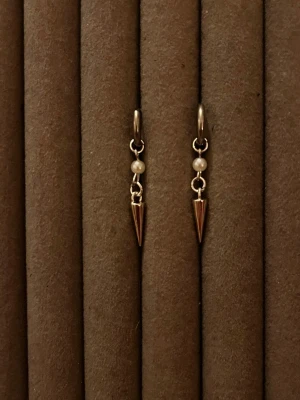 Silvriga örhängen med pärldetalj - Säljer ett par stilrena örhängen i silverfärg med små vita pärlor och spetsiga konformade hängen. Perfekta för dig som gillar minimalistisk och edgy stil. Materialet ser ut att vara metall och pärlor.