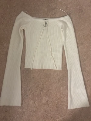 Vit ribbad offshoulder topp - står ingen direkt  storlek men skulle säga 164/xs/xss. Trendig vit ribbad topp med offshoulder-design och långa ärmar. Toppen har snörning framtill och är croppad, perfekt att styla med höga jeans eller kjol. Snygg och enkel att matcha för en cool look.