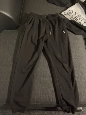 Svarta mjukisbyxor från Polo Ralph Lauren - Svarta mjukisbyxor från Polo Ralph Lauren med klassisk broderad logga på låret. Byxorna har resår och dragsko i midjan samt muddar vid bensluten. Perfekta för en chill och avslappnad stil. Tillverkade i mjukt material för extra komfort.