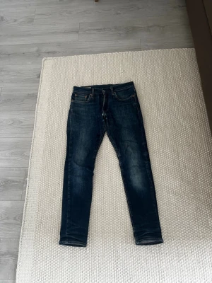 Mörkblå jeans från Levi's - Snygga mörkblå jeans från Levi's med klassiska fem fickor och diskreta slitningar. Jeansen har en straight/slim. Perfekta för en trendig och avslappnad stil.
