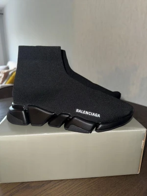 Balenciaga Speed Trainer svarta sneakers - Svarta Balenciaga Speed Trainer sneakers med stickad ovandel i stretchigt tyg och chunky sula. Minimalistisk design med vit logga på sidan och strumpliknande passform som sitter tight runt ankeln. Perfekta för dig som gillar streetwear och modern stil.