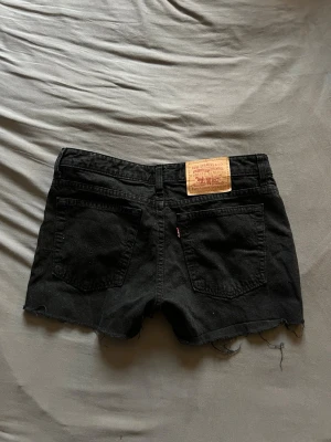 Svarta jeansshorts från Levi's - Svarta jeansshorts från Levi's med råa kanter och fickor både fram och baktill. Shortsen har en låg midja och är tillverkade i bomull. Perfekta för sommaren. 
