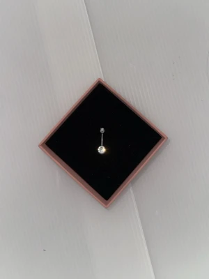 Snygg navelpiercing med kristall - Stilren navelpiercing i silverfärgad metall med två klara kristaller, en mindre och en större. Perfekt accessoar för att ge din look lite extra bling. Levereras i en rosa ask med svart insida.