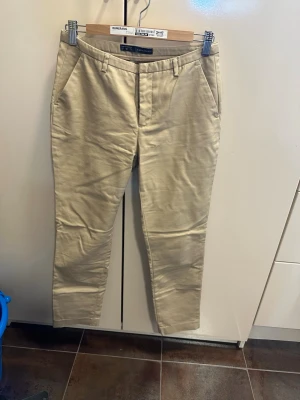 Beige kostymbyxor från Zara Basic - Snygga beige chinos från Zara Basic med klassisk rak passform och diskreta sidofickor. Tillverkade i ett mjukt bomullsmaterial som ger en skön känsla. Perfekta för en clean och stilren look. Stängs med dragkedja och knapp framtill.