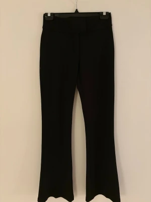 Svarta bootcut byxor - Snygga svarta bootcut byxor med hög midja och utsvängda ben. Byxorna har en enkel design utan synliga fickor framtill och är tillverkade i ett stretchigt material som ger en bekväm passform. Perfekta för en trendig och stilren look.