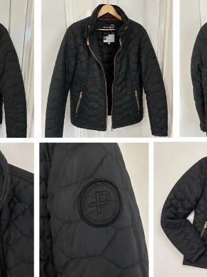 Svart pufferjacka från Pelle P - Stilren svart pufferjacka från Pelle P med quiltat mönster och svarta detaljer. Jackan har dragkedjor i bronsfärg, två fickor framtill och en diskret logotyp på ärmen. Perfekt för kalla dagar och ger en sportig vibe.