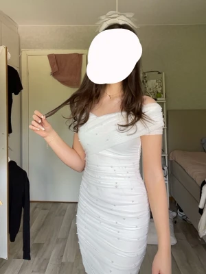 Konfirmation/student klänning - Snygg vit kort klänning med offshoulder-design och pärldetaljer.   Endast använd en gång på min konfirmation. Strl S men den kan både passa på xs och m eftersom den är så stretchig💗