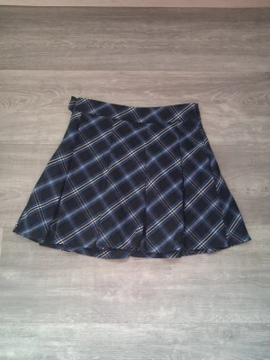 Mörkblå rutig kjol hm 32 - Snygg mörkblå kjol med blått och vitt rutmönster. Kjolen är plisserad och har en klassisk skoluniformslook med bred linning och knäppning i sidan. Perfekt för en trendig och ungdomlig stil. Kommer från h&m och är i storlek 32. Har dragkedja i sidan och en knapp