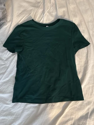 Mörkgrön basic t-shirt - En enkel mörkgrön t-shirt med rund hals och korta ärmar. Perfekt till jeans eller shorts för en clean och avslappnad look. Tillverkad i mjukt material som känns skönt mot huden. Storlek S