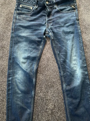 Replay jeans  - Snygga blå slim fit jeans med coola slitningar och ljusa tvättade partier. Klassisk femficksmodell med silverfärgade nitar och knapp. Perfekta för en avslappnad streetstyle-look.