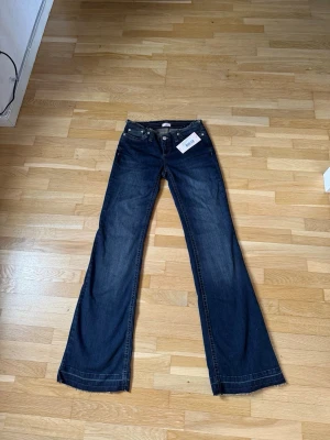 Low waist jeans från Nelly - Snygga mörkblå bootcut jeans från Nelly med rå kant i midjan och klassiska fem fickor. Jeansen har utsvängda ben och är tillverkade i denim med synliga kontrastsömmar. Perfekta för en trendig och avslappnad stil.