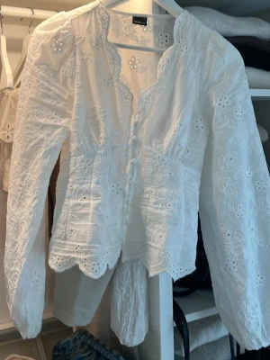 Vit trendig broderad puff-sleeve blus från Gina Tricot - Superfin vit blus från Gina Tricot med broderade blommor och scallop-kant. Blusen har lång ärm, knappar framtill och är gjord i ett tunt, luftigt material som känns som bomull. Köpt och testad men ska köpa i en större storlek💕