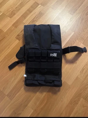 Svart viktväst från Star - Säljer en svart viktväst från Star, perfekt för träning och crossfit. Västen har justerbara remmar och flera fickor för vikter. Tillverkad i slitstarkt material och designad för att sitta bekvämt under intensiva pass. Pris kan diskuteras 