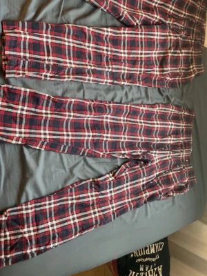 Matchande pyjamasbyxor - Säljer ett par klassiska pyjamasbyxor från 157 i rött, vitt och mörkblått rutmönster. Byxorna är i mjuk bomull och har en avslappnad passform med resår i midjan. Perfekta för mysiga hemmakvällar eller lata morgnar.