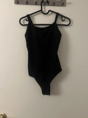 Svart ribbad body från Bik Bok - Snygg svart body från Bik Bok i storlek XS. Bodyn har smala axelband och är gjord i ett ribbat stretchigt material som sitter tajt och bekvämt. Perfekt att styla med jeans eller kjol för en clean look.