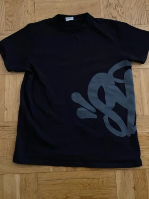 Svart t-shirt med stor grafisk print - Snygg svart t-shirt med stor grå grafisk print både fram och bak. T-shirten har klassisk passform och rund hals. Perfekt för dig som gillar streetwear och vill sticka ut med en unik design.