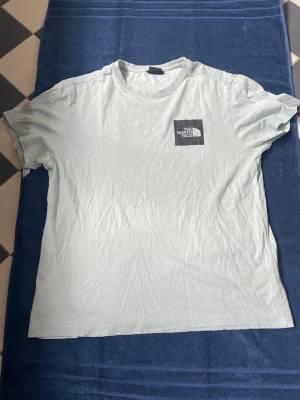Ljusgrön The North Face t-shirt - Snygg ljusgrön t-shirt från The North Face med tryckt logga på bröstet och stort grafiskt tryck på ryggen. Klassisk rund hals och korta ärmar. Perfekt för dig som gillar streetwear och outdoor-vibbar. Tillverkad i mjuk bomull för skön känsla.