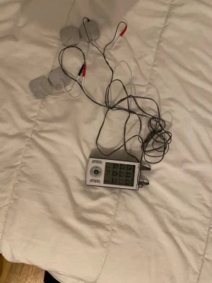 Elektrisk muskelstimulator TENS - Elektrisk muskelstimulator med fyra självhäftande elektroder och digital display. Enheten har flera program för olika kroppsdelar och styrs via knappar på framsidan. Färg: vit och svart. Perfekt för återhämtning och massage.
