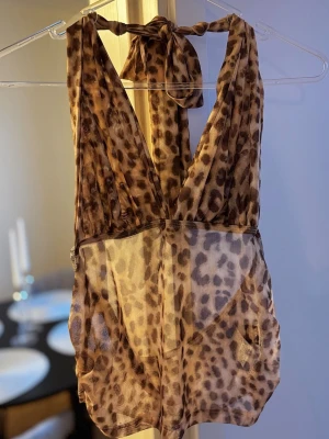 Leopardmönstrad topp - Säljer en snygg leopardmönstrad topp i mesh med djup urringning och knytning i nacken. Materialet är tunt och genomskinligt, vilket ger en trendig och sexig look. Perfekt för dig som vill sticka ut med ett djuriskt mönster.
