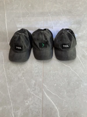Svarta kepsar med broderad logga - Tre svarta kepsar i klassisk modell med böjd skärm och broderad logotyp framtill. Två kepsar har TCL-logga i vitt på svart patch, en har en grön symbol på svart patch. Justerbar passform baktill. Materialet ser ut att vara bomull.
