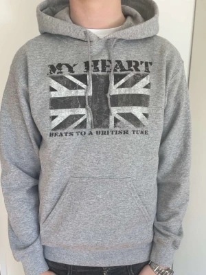 Grå Hoodie från Drakenberg - Säljer en riktigt fet och go grå hoodie från Drakenberg. På bröstet finns ett stort tryck av Union Jack-flaggan och texten 'MY HEART BEATS TO A BRITISH TUNE'. Hoodien har ribbade muddar vid ärmar och nederkant. Nypris 929kr. Använd kanske 3 gånger. Skickar snabbt, pris är mycket diskuterbart vid smidig affär.