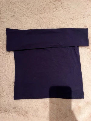 Mörkblå axelbandslös tubtopp - Säljer en enkel och stilren mörkblå tubtopp som är axelbandslös och har en bred kant upptill. Perfekt att matcha med jeans eller kjol för en clean look. Materialet känns mjukt och stretchigt.