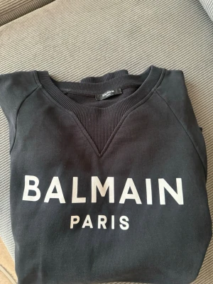 Svart sweatshirt från Balmain  - Svart sweatshirt från Balmain i storlek M. Tröjan är i gott använt skick, den kan behövas tvättas (se bilder), samt att halskragen är lite uttöjd. Hör av er vid intresse eller vid önskan om fler bilder!