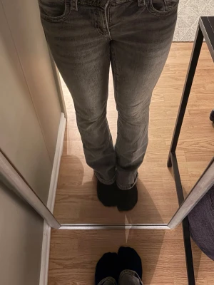 Grå bootcut jeans med fickdetaljer - Säljer ett par grå bootcut jeans med klassisk fyrficksmodell och snygga fickdetaljer bak. Jeansen har en lätt tvättad look och låg midja. Perfekta för dig som gillar en avslappnad men trendig stil.